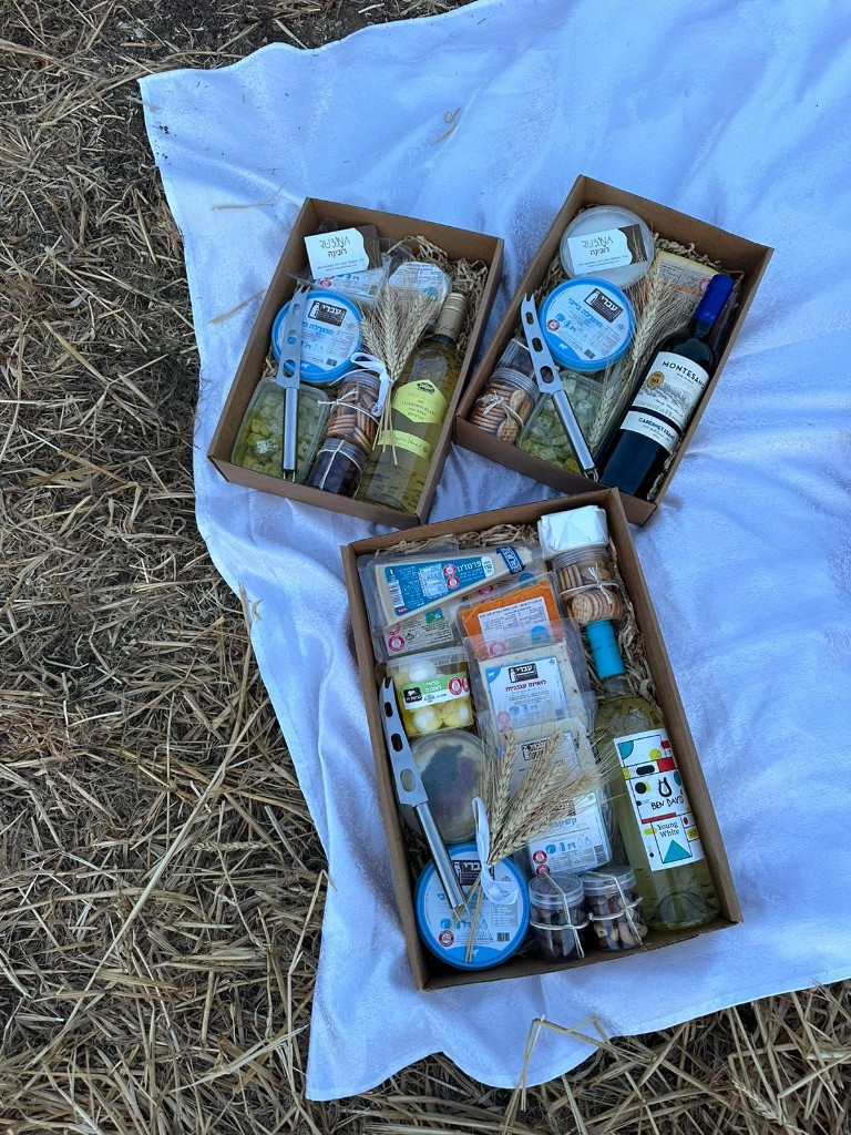 שלושה מארזים פתוחים עם גבינות ויין על מפה לבנה